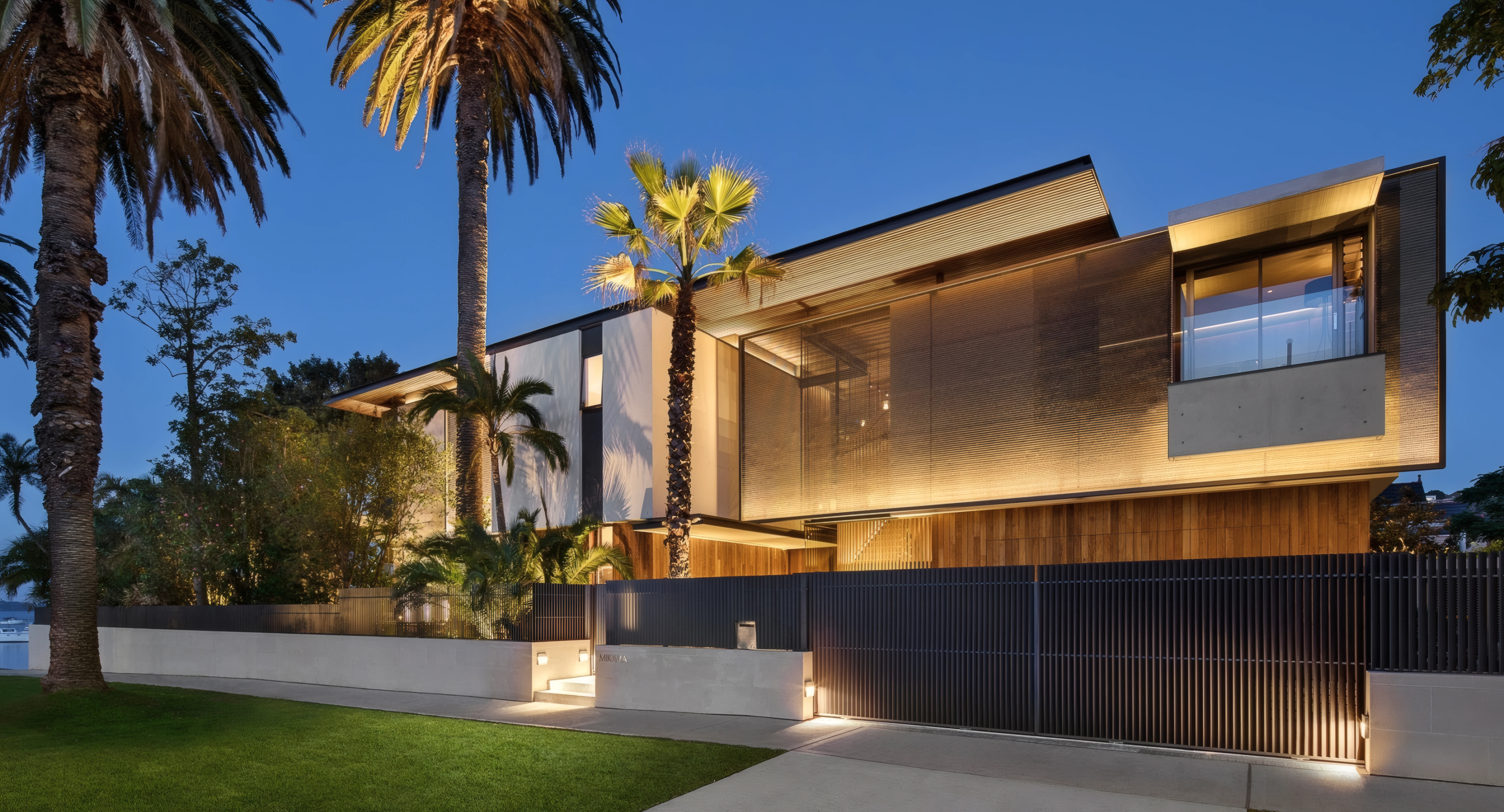 Modern two-storey home at dusk with uplit palm trees, a glowing timber and mesh facade, and low garden wall lights along the entrance